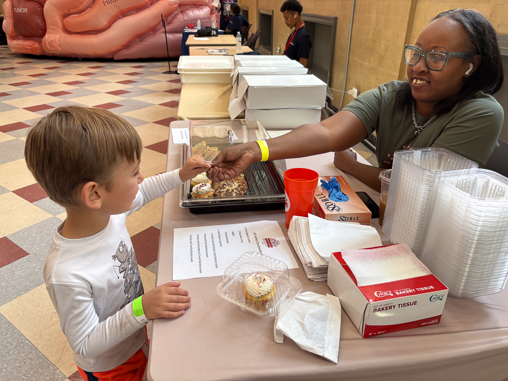 At a birthday table, a woman gives a cupcake to a child while they exchange a Breadcoin.
